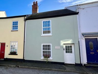 A street view of three attached houses with different colored doors one labeled Pilchard Cottage in Dawlish