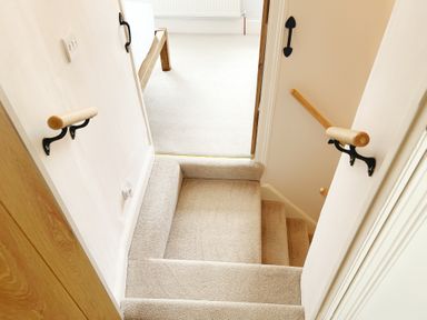 Carpeted staircase with wooden handrails leading to a carpeted room with a wooden bed frame at Pilchard Cottage in Dawlish