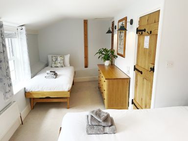 A bedroom with two single beds a wooden dresser and a wooden door at Pilchard Cottage in Dawlish
