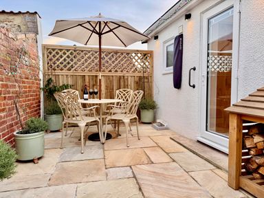 An outdoor patio with a table and four chairs under an umbrella and potted plants at Pilchard Cottage in Dawlish