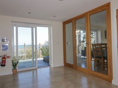 A room with tiled floor sliding glass door leading outside and wooden framed glass doors reflecting a dining area at Lower Mellan Barn in Coverack