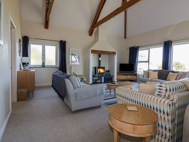 A living room with sofas a fireplace a television and wooden tables at Lower Mellan Barn in Coverack