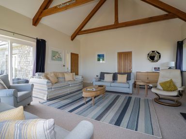 A living room with sofas armchairs wooden beams and a striped rug at Lower Mellan Barn in Coverack