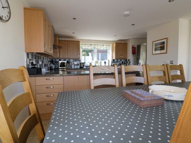 A kitchen with wooden cabinets a dining table with polka dot tablecloth and wooden chairs at Lower Mellan Barn in Coverack