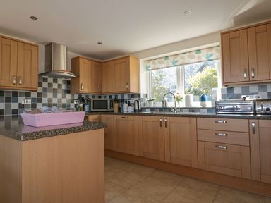 A kitchen with wooden cabinets a tiled backsplash a stainless steel hood microwave toaster and a window at Lower Mellan Barn in Coverack