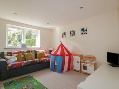 A playroom with a sofa covered by a star-patterned blanket pillows a red and white play tent children's kitchen set and a small television at Lower Mellan Barn in Coverack