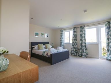 A bedroom with a bed, a desk with a vase, windows with patterned curtains at Lower Mellan Barn in Coverack