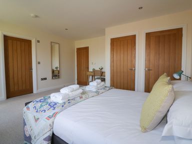 A bedroom with a bed having folded towels and a decorative runner with three wooden doors and a small desk with a chair at Lower Mellan Barn in Coverack