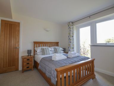 A bedroom with a wooden bed frame two bedside tables with lamps folded towels on the bed and a large window with patterned curtains at Lower Mellan Barn in Coverack