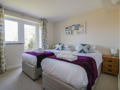 A bedroom with two single beds each with purple throws and folded towels near a window at Lower Mellan Barn in Coverack