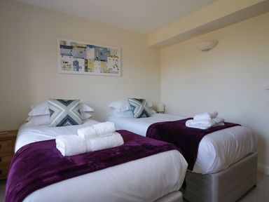 A bedroom with two single beds with white linens purple throws and folded towels at Lower Mellan Barn in Coverack