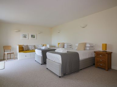 A bedroom with two single beds a wooden nightstand and a seating area at Lower Mellan Barn in Coverack