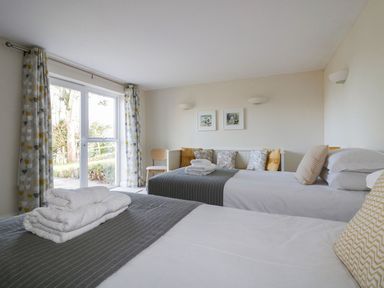 A bedroom with two beds folded towels on one bed curtains on a window and cushions on a bench at Lower Mellan Barn in Coverack