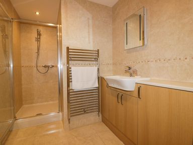 A bathroom with a shower enclosure a towel radiator a sink with a cabinet and a mirror at Lower Mellan Barn Coverack