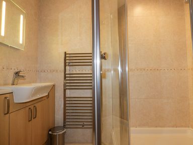 A bathroom with a sink cabinet a towel radiator and a glass shower at Lower Mellan Barn in Coverack