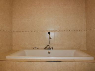 A bathroom with a built-in bathtub and tiled walls at Lower Mellan Barn in Coverack