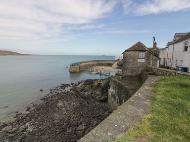 A small coastal harbor with fishing boats moored near a stone pier and old buildings at Lower Mellan Barn in Coverack