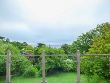 A garden with trees and grass seen through a glass and wooden balcony railing at Lower Mellan Barn in Coverack