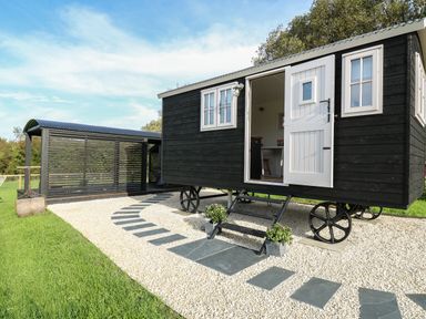 A black wooden shepherds hut with white door and windows on gravel with a stone pathway at Dragonfly Shepherd's Hut in Oakford near Aberaeron