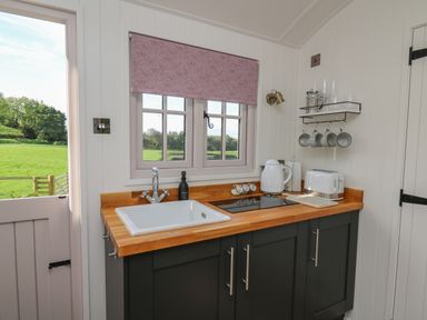 A kitchen with a sink stove kettle and toaster under a window with a view of a green field at Dragonfly Shepherd's Hut Oakford near Aberaeron