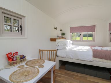 A bedroom with a bed next to windows and a small table with chairs at Dragonfly Shepherd's Hut in Oakford near Aberaeron