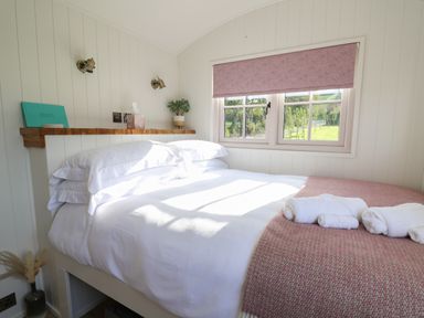A bedroom with a made bed with white sheets towels on a pink blanket by a window at Dragonfly Shepherd's Hut in Oakford near Aberaeron