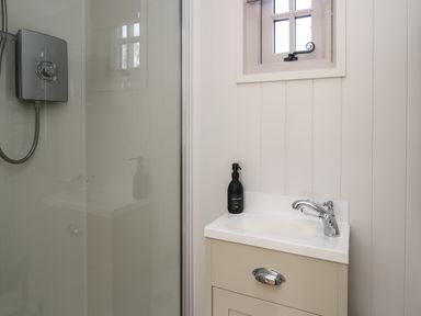 A bathroom with a shower, sink, hand soap, and a small window at Dragonfly Shepherd's Hut Oakford near Aberaeron
