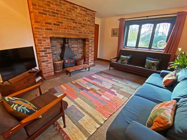 A living room with a brick fireplace wooden chairs sofas a colorful rug and a television at Rivendell in Weybread near Harleston