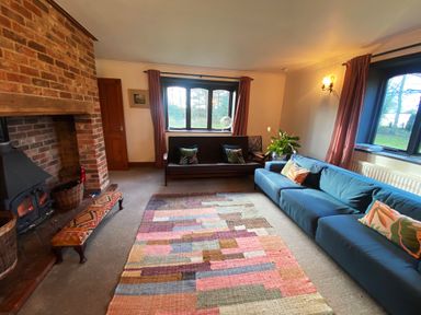 A living room with a brick fireplace blue and brown sofas a colorful rug and windows with curtains at Rivendell in Weybread near Harleston