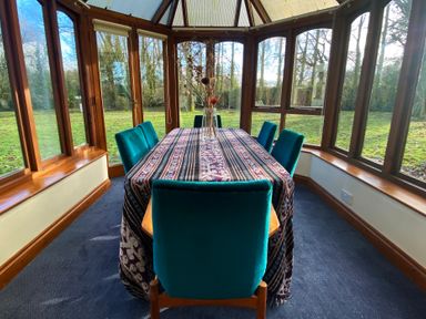 A dining area with a table covered by a patterned cloth and six chairs inside a conservatory at Rivendell Weybread near Harleston