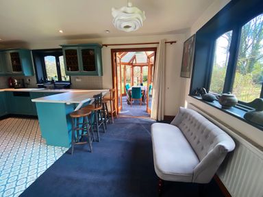 A kitchen with blue cabinets and a breakfast bar with stools leading to a dining area with a table and chairs at Rivendell Weybread near Harleston