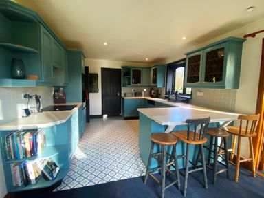 A kitchen with blue cabinets a tiled floor and wooden stools at a counter at Rivendell in Weybread near Harleston