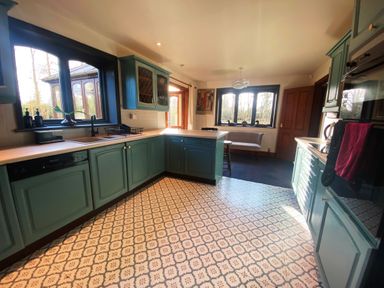 A kitchen with teal cabinets a patterned floor and windows with a sitting area at Rivendell in Weybread near Harleston