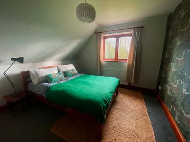 A bedroom with a bed a lamp a window with curtains and a patterned wallpaper at Rivendell in Weybread near Harleston