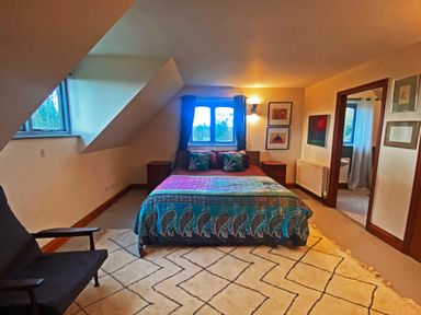 A bedroom with a bed with colorful bedding a chair a carpet and bathroom access at Rivendell in Weybread near Harleston