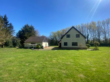 A house with a detached garage on a grassy lawn surrounded by trees at Rivendell in Weybread near Harleston