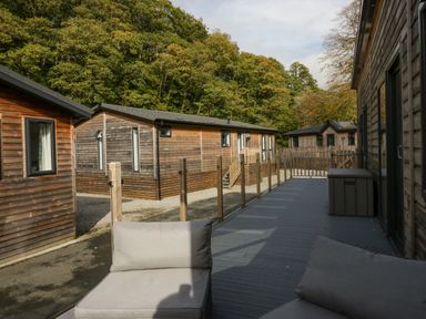 A deck with outdoor chairs and a storage box next to wooden cabins and trees in the background at The Bothy in Keswick