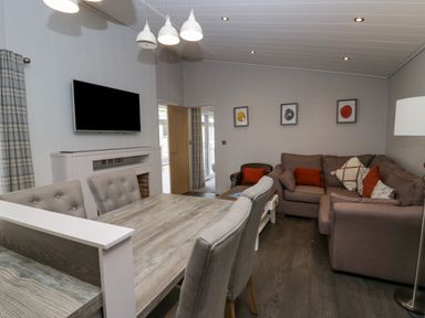 A living room with a dining table chairs sofa and wall mounted TV at The Bothy in Keswick