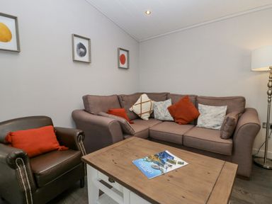A living room with a brown leather armchair and a beige sofa with cushions a wooden coffee table and floor lamp at The Bothy in Keswick