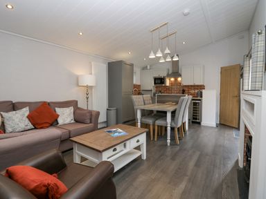 A living area with a sofa and armchair a wooden coffee table and a dining table with four chairs near a kitchen at The Bothy in Keswick