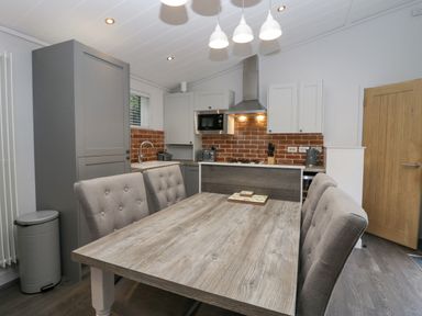 A kitchen and dining area with a wooden table and padded chairs at The Bothy in Keswick