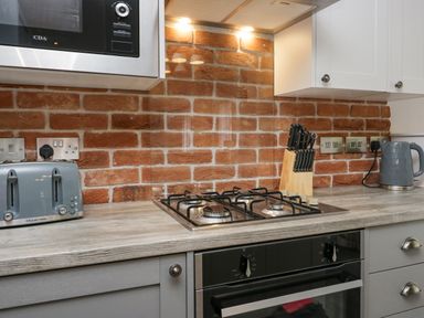 A kitchen countertop with a gas stove knives toaster kettle and microwave above against a brick wall at The Bothy in Keswick
