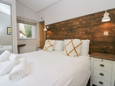 A bedroom with a bed with white linens and two patterned pillows a wooden headboard and a bedside table at The Bothy in Keswick