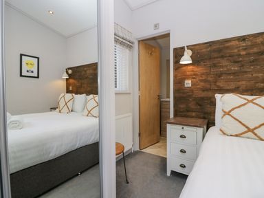 A bedroom with a double bed with cushions a bedside table a wall lamp a window with blinds and a door leading to another room at The Bothy in Keswick