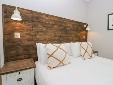 A bed with white bedding and two patterned pillows with wooden headboard and bedside tables at The Bothy in Keswick