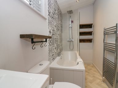 A bathroom with a bathtub shower and patterned wall tiles at The Bothy in Keswick