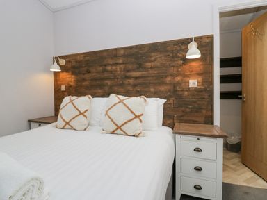 A bedroom with a bed featuring two pillows and a wooden headboard flanked by two bedside tables with lamps at The Bothy in Keswick