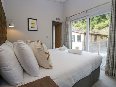 A bedroom with a bed with white linens and pillows next to a glass door with curtains at The Bothy in Keswick