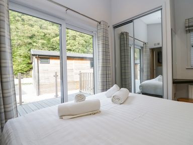 A bedroom with a bed and rolled towels near glass sliding doors and a mirrored wardrobe at The Bothy in Keswick