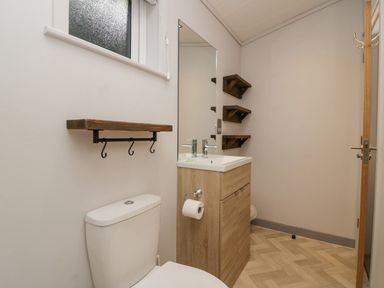 A bathroom with a toilet a sink with wooden cabinet a mirror and wooden shelves at The Bothy in Keswick